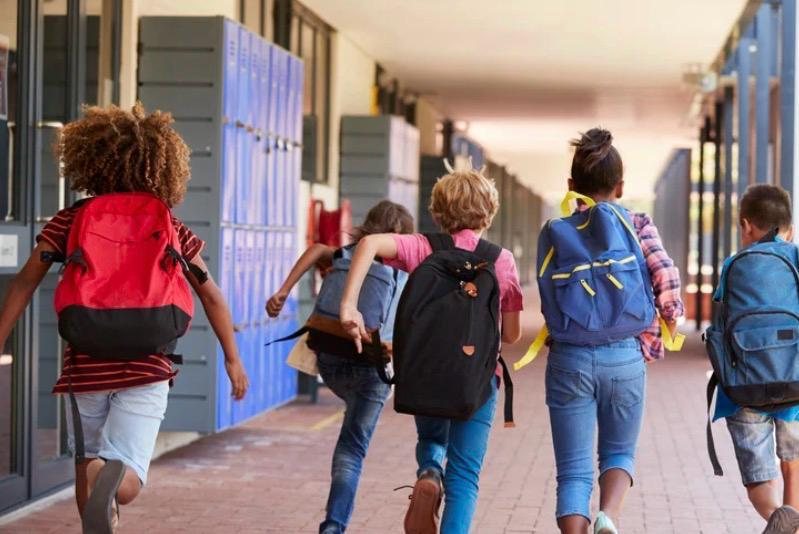 Schulkinder mit Rucksäcken laufen durch einen Flur
