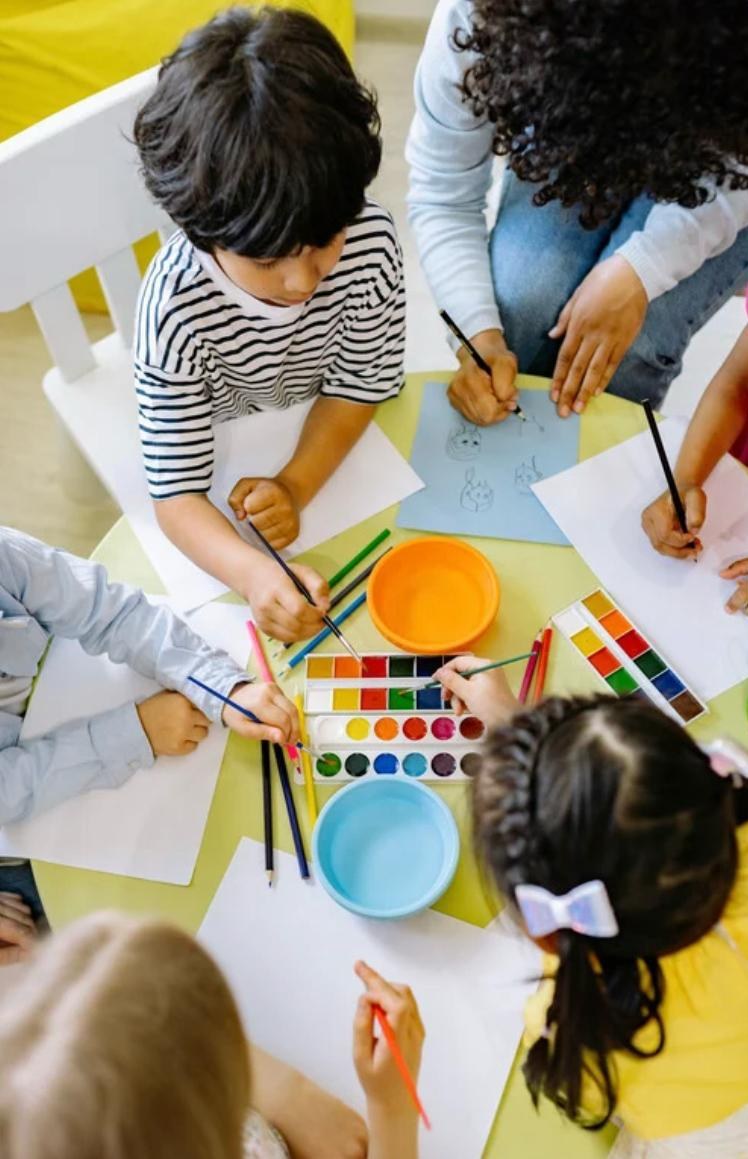 Kinder malen gemeinsam mit Wasserfarben am Tisch